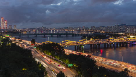 Blick-Auf-Die-Nächtliche-Verkehrsskyline-Von-Seoul,-Zeitraffer-Des-Verkehrs-Auf-Der-Autobahn-Olympic-Daero,-Die-Eisenbahnbrücken-über-Den-Han-Fluss-Und-Den-Hangang-Und-Einen-Dunklen,-Dramatischen-Himmel