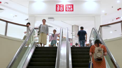 Los-Compradores-Chinos-Suben-Las-Escaleras-Mecánicas-En-Un-Centro-Comercial-De-Hong-Kong,-Dirigiéndose-Hacia-La-Tienda-Uniqlo-De-La-Marca-Japonesa