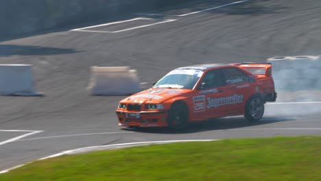 Orangefarbener-BMW-Driftet-Mit-Einem-Blauen-BMW-In-Einer-Engen-Kurve-Mit-Viel-Rauch