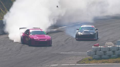 two-race-cars-drifting-on-a-very-tight-curve-followed-by-a-drone-through-all-the-smoke