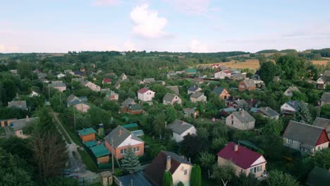 Aerial-footage-of-a-Baltic-summerhouse-village-showcasing-charming-houses-with-gardens-surrounded-by-lush-greenery-and-rolling-hills-under-a-clear-blue-sky