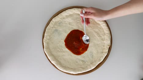 Spreading-Tomato-Sauce-On-A-Dough-Pizza-Base-Using-A-Spoon,-Closeup-Shot