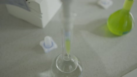 Eine-Laborpipette-Dosiert-Flüssigkeit-In-Einen-Kolben-Auf-Einem-Labortisch