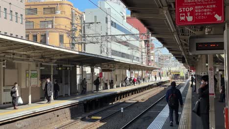 Una-Vista-De-Una-Estación-De-Metro-En-Kioto,-Japón,-Revela-Una-Plataforma-Limpia-Y-Moderna-Con-Trenes-Elegantes,-Señalización-Clara-Y-Pasajeros-Bulliciosos.