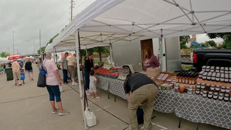 customers-shopping-at-a-farmer's-market-display-of-fresh,-locally-harvested-raw-honey-and-vegetables-at-summer-farmer's-market