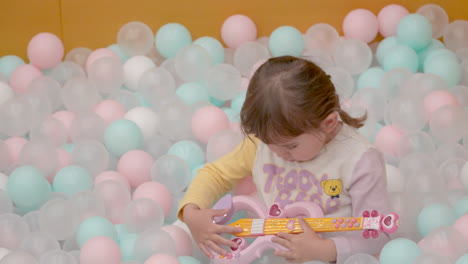 Linda-Niña-Pequeña-Tocando-Una-Guitarra-De-Juguete-En-Una-Piscina-De-Bolas-De-Colores-En-Cámara-Lenta