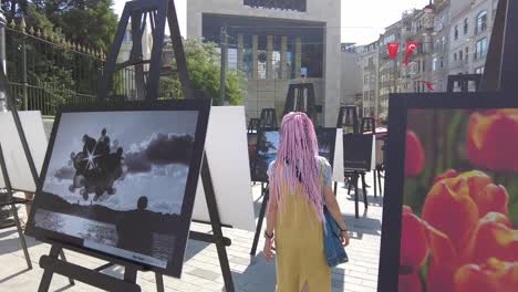 Un-Visitante-Pasea-Por-Una-Exposición-De-Pinturas-En-La-Plaza-De-Estambul,-Capturando-La-Esencia-De-La-Apreciación-Artística-Y-El-Compromiso-Cultural.