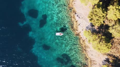 Top-aerial-drone-shot-of-a-small-boat-floating-on-blue-turquoise-sea-water-near-the-coast