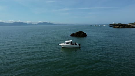 Aerial-view-circling-small-fishing-boat-anchored-off-coast-of-Ynys-Llanddwyn-idyllic-Welsh-island