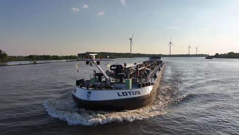 Buque-De-Carga-En-órbita-Sobre-Un-Río-Tranquilo-Con-Turbinas-Eólicas-De-Fondo,-Transporte-Sostenible,-Libertad-De-Comercio-Mundial