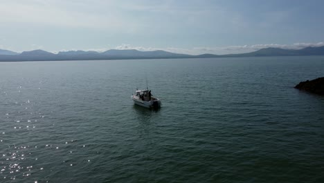 Vista-Aérea-De-Un-Pequeño-Barco-Pesquero-Anclado-En-La-Resplandeciente-Costa-De-Ynys-Llanddwyn,-Una-Idílica-Isla-Galesa