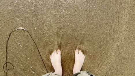 Männerfüße-Stehen-Im-Sand-Und-Wellen-Schlagen-über-Ihre-Füße