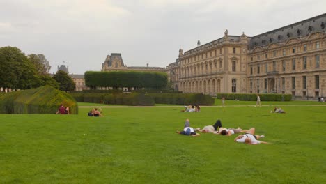 People-relax-on-the-green-lawn-outside-the-Louvre-museum-in-Paris,-France