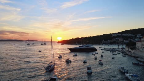 Toma-Aérea-Con-Dron-De-Una-Bahía-Llena-De-Barcos-De-Vela-Durante-La-Puesta-De-Sol-En-La-Isla-De-Hvar,-Croacia