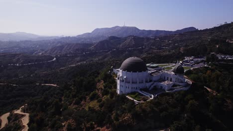 Impresionante-Toma-Aérea-Del-Observatorio-Griffith-Ubicado-En-Las-Colinas-De-Los-Ángeles,-Que-Muestra-El-Emblemático-Monumento-Con-El-Telón-De-Fondo-De-La-Extensa-Ciudad-Y-Las-Montañas-Circundantes.