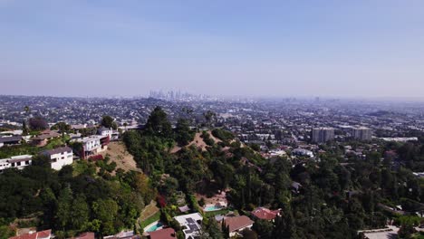 Stunning-aerial-footage-showcasing-hillside-homes-with-a-breathtaking-view-of-Los-Angeles'-expansive-urban-landscape,-captured-under-a-clear-blue-sky