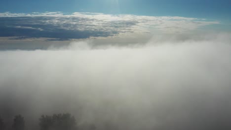 Aerial-ascend-through-dense-morning-fog-to-clear-and-bright-sky-view,-Latvia