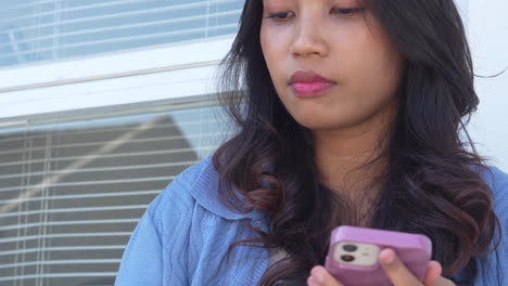 Mujer-Joven-Asiática-Usando-Un-Teléfono-Inteligente-Mientras-Come-Un-Pastel-De-Tiramisú-En-Una-Cafetería