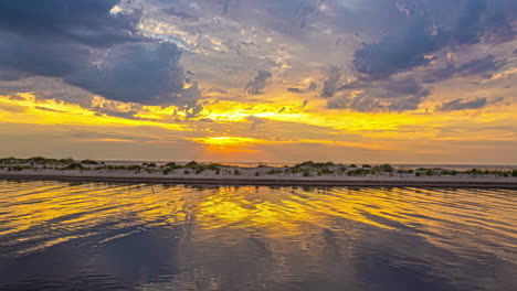 Canal-water-reflects-a-golden-sunset-cloudscape-by-a-beach---time-lapse