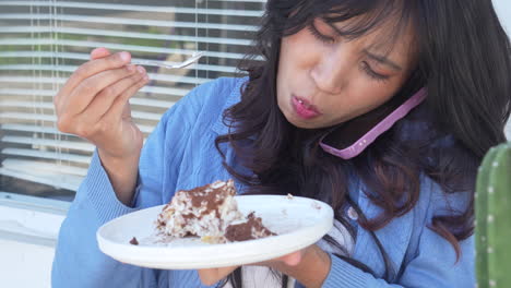 Junge-Asiatische-Frau,-Die-Auf-Dem-Smartphone-Spricht-Und-Dabei-Tiramisu-Kuchen-Genießt