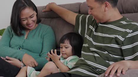 Padres-Vigilando-A-Su-Pequeña-Hija-Usando-Un-Teléfono-Inteligente-En-Casa