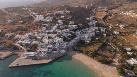 Aéreo-Estableciendo-órbita-Sobre-Playa-De-Arena-Con-Agua-Clara-A-Donousa-Grecia-Casas-En-La-Ladera-De-La-Montaña