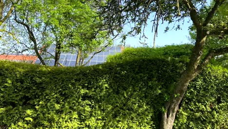 Tracking-shot-of-red-brick-farm-House-with-modern-solar-panels-between-green-trees-and-hedge