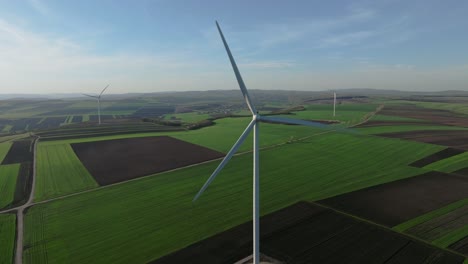 Wind-turbines-spinning-in-a-vast-green-field-on-a-sunny-day,-aerial-view