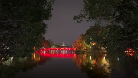 Red-Bridge-at-night-bottom-of-frame---The-Huc-Bridge-over-Hoan-Kiem-Lake,-Hanoi,-Vietnam