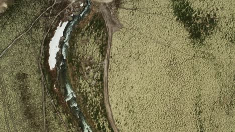 Drone-zenithal-view-follows-flow-of-Storula-River-below-footbridge-and-winding-paths-in-Rondane-National-Park-Innlandet-county-Norway