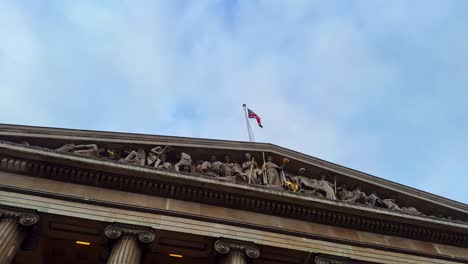 Waving-United-Kingdom-flag-on-top-of-British-Museum-in-London,-clear-skyline