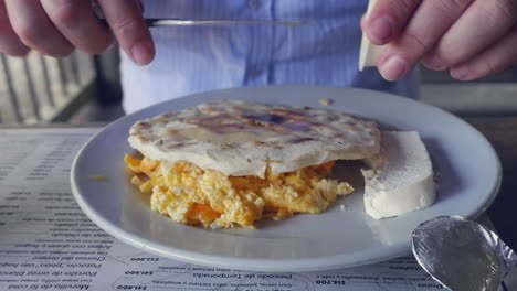 Man-puts-butter-on-Huevos-Montaneros,-traditional-latin-breakfast-meal