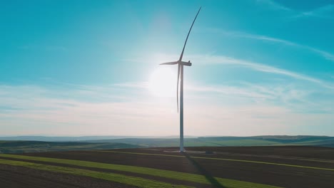 Wind-turbine-spinning-in-a-vast,-sunny-field-with-clear-blue-skies