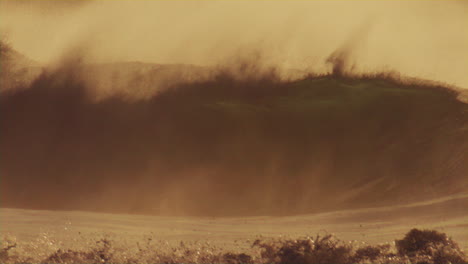 Front-view-of-lip-crashing-onto-surface-as-soft-early-morning-light-dances-across-waves-as-offshore-winds-pull-ocean-spray-mist-over-top