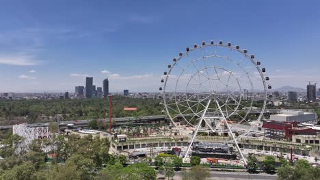 Jib-up-drone-overlooking-the-Wheel-of-Fortune-in-Aztlan-Park,-revealing-Bosque-de-Chapultepec,-Mexico-City