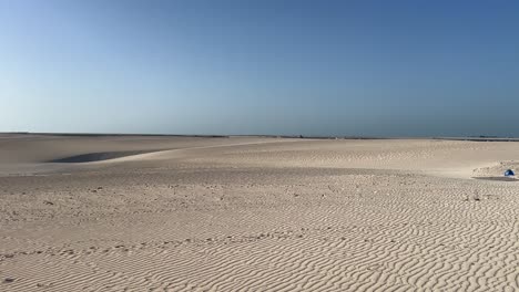 Lens-flare-from-afternoon-sun-over-scattered-sand-dunes-in-hot-desert