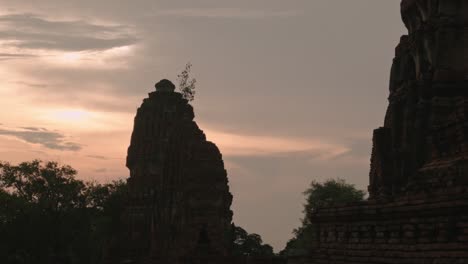 Birds-fly-over-Wat-Ratchaburana-Ayutthaya,-magical-purple-and-orange-sunset