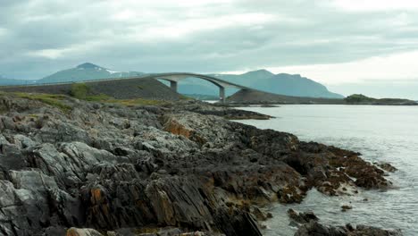 Drone-establishing-dolly-above-jagged-rocks-to-Atlanterhavsvegen-bridge-in-Nordmore,-Norway