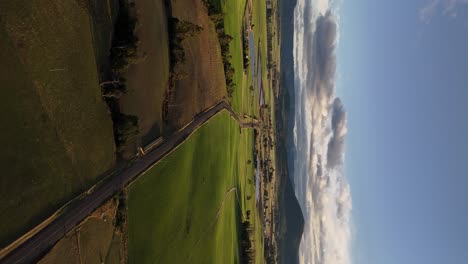 Vertical-drone-shot-of-green-landscape-with-road-in-Tasmania,-Australia