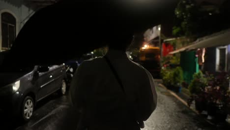 Person-walking-on-a-rainy-street-at-night-holding-an-umbrella