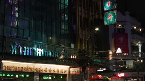 Neon-signs-illuminate-Chinatown-at-night,-reflecting-off-the-glass-buildings