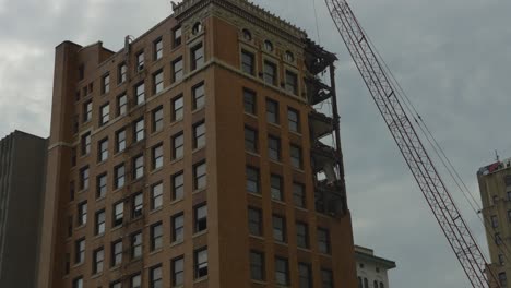 A-high-rise-building-in-Youngstown,-Ohio,-undergoing-demolition,-with-a-visible-crane-and-partially-dismantled-upper-floors,-showcasing-the-transformation-of-the-urban-landscape