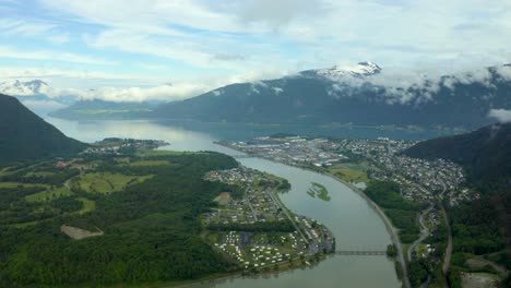 Panoramic-aerial-establishing-view-of-Andalsnes-in-Rauma-Norway-with-beautiful-clouds-surrounding-snow-capped-mountains