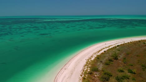 Drone-shot-of-clear-turquoise-water-meeting-a-pristine-white-sand-beach