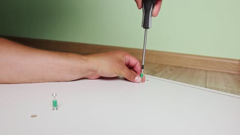 Hands-with-screwdriver-and-screw-assembling-furniture,-work-in-room-interior