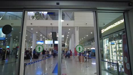 Entering-Tbilisi-Airport,-Georgia,-passing-through-glass-sliding-doors-to-reveal-a-line-of-people-waiting-for-luggage-and-tickets