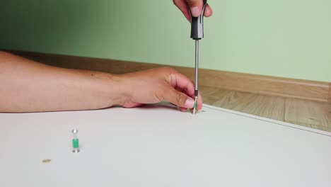 Close-up-on-hands-with-screwdriver-and-screw,-assembling-furniture-at-home