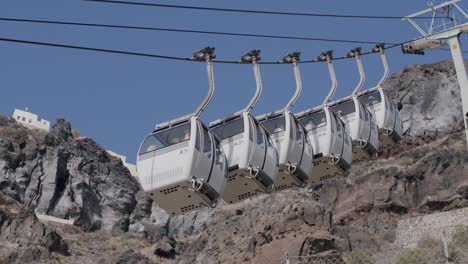 Cable-cars-ascending-rocky-cliffs-in-Fira,-Santorini,-Greece-under-a-clear-blue-sky