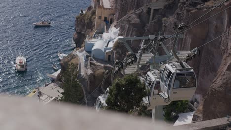 Cable-cars-ascending-steep-cliffs-in-Fira,-Santorini,-Greece-during-a-sunny-day