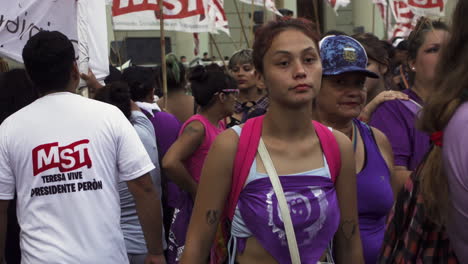 close-shot-of-young-female-advocate-during-peaceful-women's-day-march-wearing-purple-clothes,-flags-wave-in-background